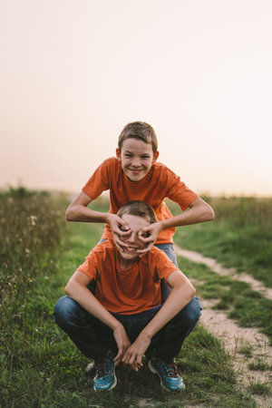 Funny twin brother boys playing outdoors on field at sunset.の写真素材