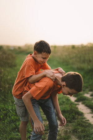 Funny boys brothers in a orange T-shirt playing outdoors on the field at sunsetの写真素材