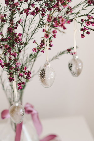 Easter eggs hang on a sprig of flowers in a transparent vase.
