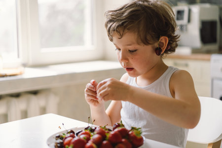 Cute beautiful little boy eating fresh cherry and strawberry.の写真素材
