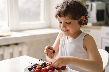 Cute beautiful little boy eating fresh cherry and strawberry.の写真素材