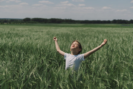 Portrait of a boy in a white T-shirt and playing in a green barley field.の写真素材