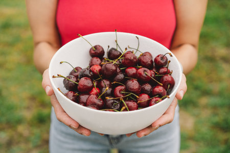 The girl is holding a large plate of ripe cherries.