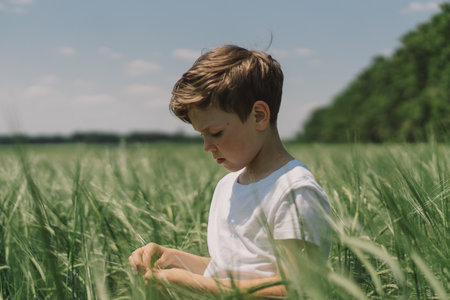 Portrait of a boy in a white T-shirt and playing in a green barley field.の写真素材