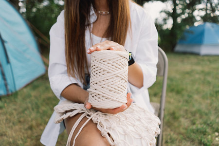 Woman knits bag using macrame technique outdoors near tents. Outdoor hobbies.の写真素材
