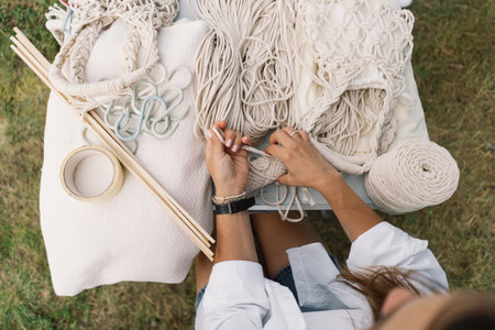 Woman knits bag using macrame technique outdoors near tents. Outdoor hobbies.