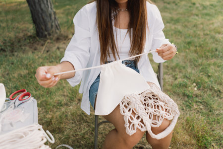 Woman knits bag using macrame technique outdoors near tents. Outdoor hobbies.
