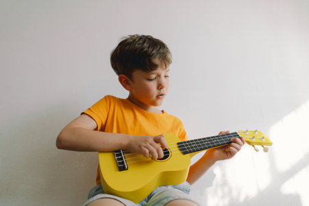 Cute boy learns to play the yellow Ukulele guitar in home. Cozy home.の写真素材