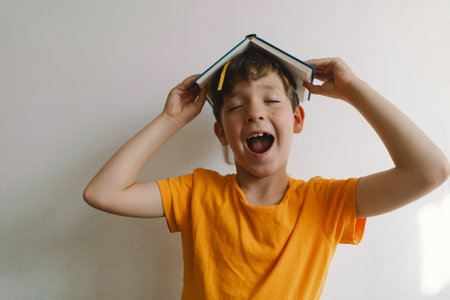 A cute boy wearing an orange T-shirt is sitting on a soft ottoman reading a book