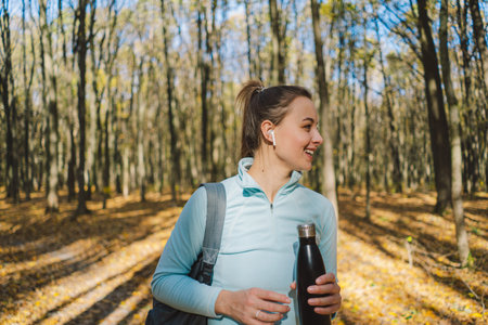 The girl drinks water. A beautiful girl is doing fitness outdoors in a sunny autumn forest