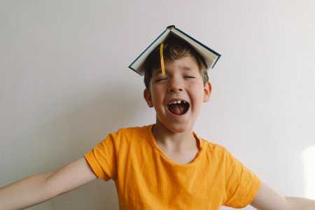 A cute boy wearing an orange T-shirt is sitting on a soft ottoman reading a bookの写真素材
