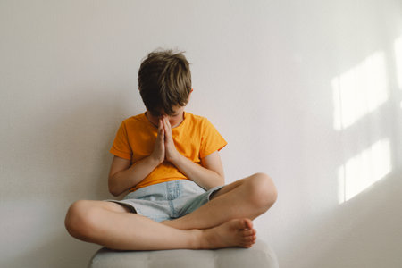 A boy in an orange T-shirt prays at home. Concept for faithの写真素材