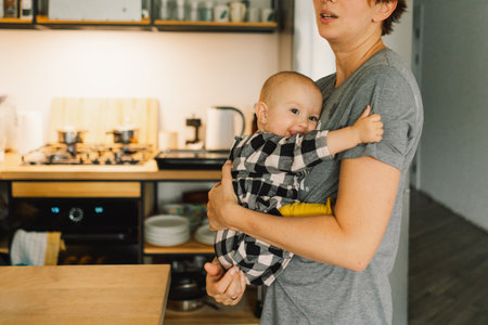 A mother holds her daughter in her arms in the kitchen.の写真素材
