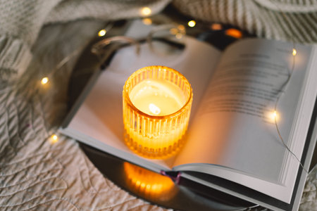 Scented candle with an open book in bed with a warm blanketの写真素材