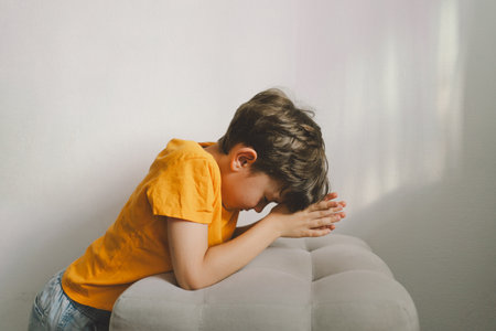 A boy in an orange T-shirt prays at home. Concept for faithの写真素材