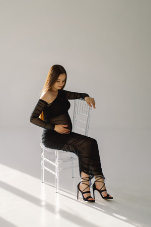 Cute young Pregnant girl sitting on the white studio in warm lightの写真素材