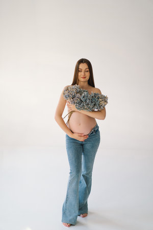 Cute young Pregnant girl sitting on the white studio in warm lightの写真素材