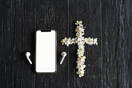 Spring flowers in the shape of a cross, a phone with headphones on an old wooden backgroundの写真素材