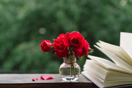 Bouquet of red rose in a vase and a book on a wooden window sill.の写真素材
