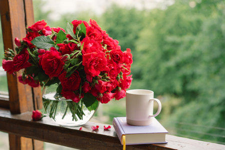 Bouquet of red rose in a vase and a book on a wooden window sill.の写真素材