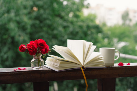 Bouquet of red rose in a vase and a book on a wooden window sill.の写真素材