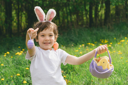 Boy with eggs basket and bunny ears on Easter egg hunt in sunny spring garden.の写真素材