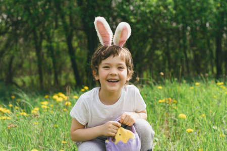 Boy with eggs basket and bunny ears on Easter egg hunt in sunny spring garden.の写真素材