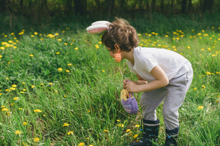 Boy with eggs basket and bunny ears on Easter egg hunt in sunny spring garden.の写真素材