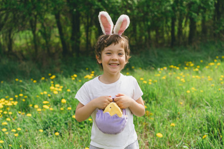 Boy with eggs basket and bunny ears on Easter egg hunt in sunny spring garden.の写真素材