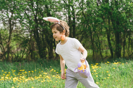 Boy with eggs basket and bunny ears on Easter egg hunt in sunny spring garden.の写真素材