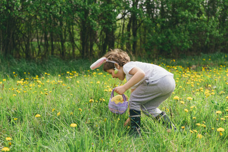 Boy with eggs basket and bunny ears on Easter egg hunt in sunny spring garden.の写真素材