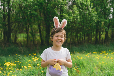 Boy with eggs basket and bunny ears on Easter egg hunt in sunny spring garden.の写真素材