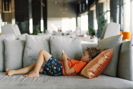 A boy with curly hair is deeply immersed in the game on the phone.の写真素材