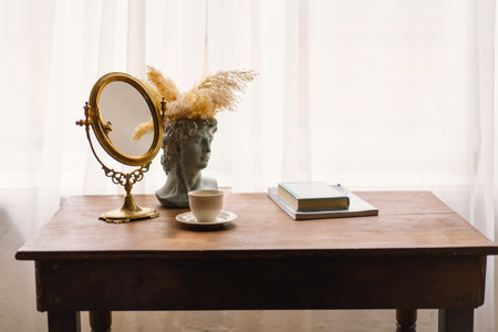 Elegant Vintage Mirror and Bust Vase With Pampas Grass Next to a Coffee Cup on a Wooden Tableの写真素材