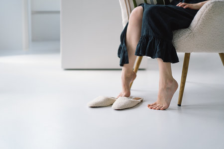 Woman Sitting on Sofa Removing Slippers in a Bright Living Roomの写真素材