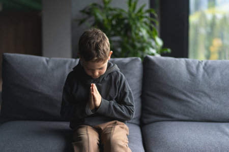 Young Boy Sitting on a Sofa With Hands Clasped in a Moment of prayingの写真素材