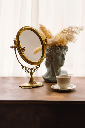 Elegant Vintage Mirror and Bust Vase With Pampas Grass Next to a Coffee Cup on a Wooden Table