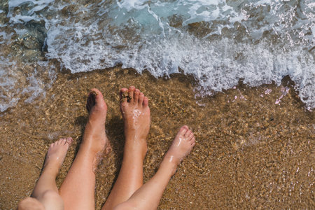 The feet of mother and son are positioned close together on the ocean shorehの写真素材