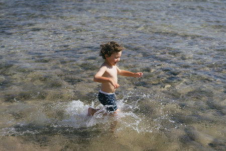 Young Boy Running Through Shallow Ocean Water On Sunny Dayの写真素材
