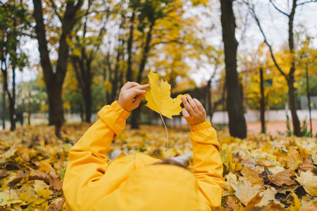 Joyful Child in Yellow Raincoat Laying in Autumn Leaves at a Park