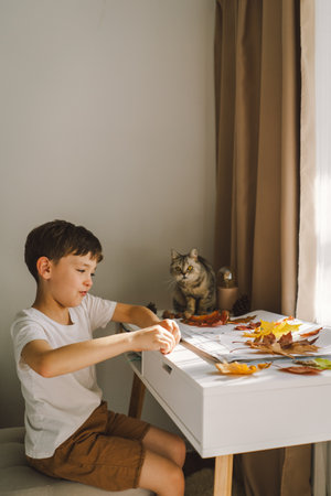 Boy Engaged in Creative Leaf Art Activity at Home with catの写真素材