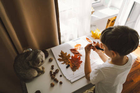 Boy Engaged in Creative Leaf Art Activity at Home with catの写真素材