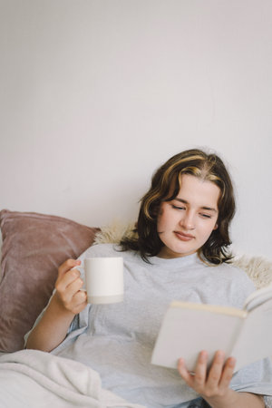 Young woman reading a book while sipping coffee at home