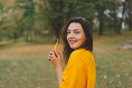 A woman enjoys a autumn day while playfully holding a yellow leafの写真素材