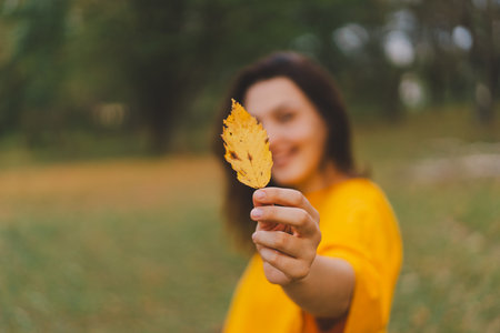 A woman enjoys a autumn day while playfully holding a yellow leaf