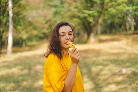 A woman enjoys a autumn day while playfully holding a yellow leafの写真素材
