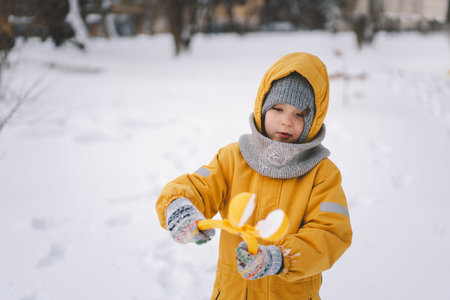 Young boy playing with a snowball maker in a cold winter day