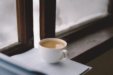 Cozy winter day with steaming coffee, open book, and candlelight by the snowy windowの写真素材