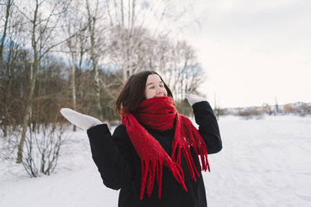 A woman with a red scarf enjoys a snowy winter day in a forest setting beneath a bright blue skyの写真素材