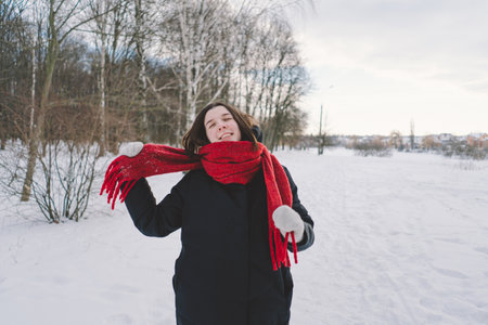 A woman with a red scarf enjoys a snowy winter day in a forest setting beneath a bright blue sky